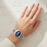 Blue cat's eye 58.55ct Hand wearing a silver bracelet with a blue stone on a marble surface