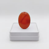 natural red agate carnelian aqeeq 37.10ct Red oval stone on a white box against a white background
