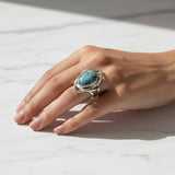 nishapur turquoise 74.90ct Hand wearing a silver ring with a turquoise stone on a light background