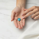 nishapur turquoise 27.29ct stone held between two hands on a white fabric background
