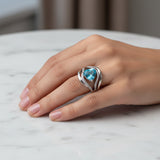 swiss blue topaz trillion 31.60ct Hand wearing a ring with a blue gemstone on a marble surface