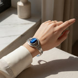 61.80ct cat eye stone Hand wearing a silver bracelet with a blue stone, against a neutral background.