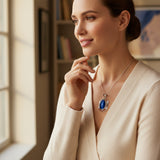 cats eye stone 57.35ct Woman wearing a necklace with a blue pendant in a room with a window and bookshelf.
