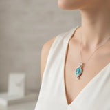 nishapur turquoise 27.29ct Necklace with a blue pendant worn by a person in a white dress against a neutral background