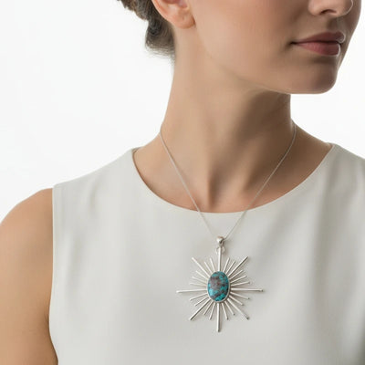 nishapur turquoise 36.35ct Woman wearing a necklace with a sunburst pendant and turquoise stone on a white background