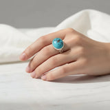 nishapur turquoise 27.29ct Hand wearing a turquoise ring on a white fabric background