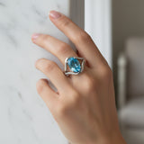 swiss blue topaz round stone 29.05ct Hand wearing a ring with a blue gemstone on a neutral background