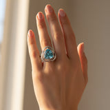 swiss blue topaz round stone 29.20ct Hand wearing a ring with a blue gemstone against a neutral background