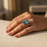 swiss blue topaz round stone 33.75ct  Hand wearing a ring with a blue gemstone on a beige surface