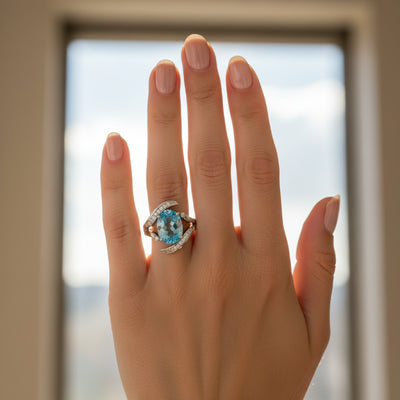 swiss blue topaz round stone 43.70ct  Hand wearing a ring with a blue gemstone against a blurred background