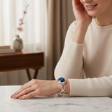 cat eye 59.50 ct Woman wearing a silver bracelet with a blue gemstone on a marble surface.