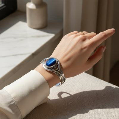 61.80ct cat eye stone Hand wearing a silver bracelet with a blue stone, against a neutral background.