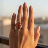natural red agate carnelian aqeeq 31.15ct Hand wearing a ring with a red stone against a blurred background