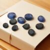 Collection of 10 natural blue sapphire gemstones totaling 17 carats, featuring oval and pear shapes with deep blue and dark tones, displayed on a white background, promoted by Abellario